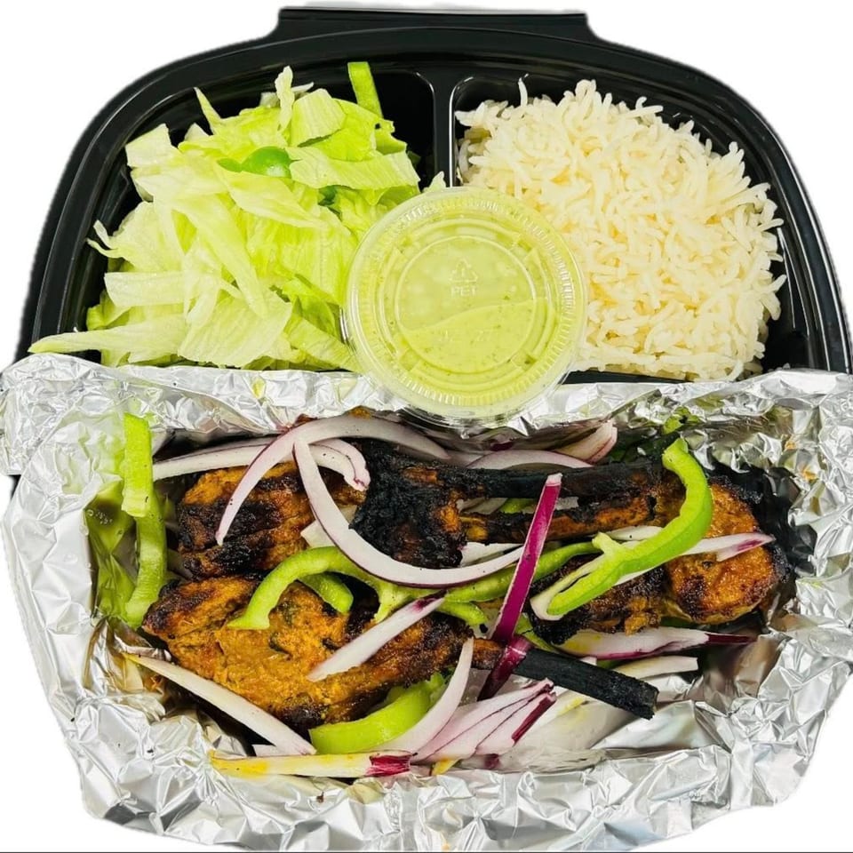 Grilled chicken with onions and peppers, rice, lettuce, and green sauce in a takeout container.