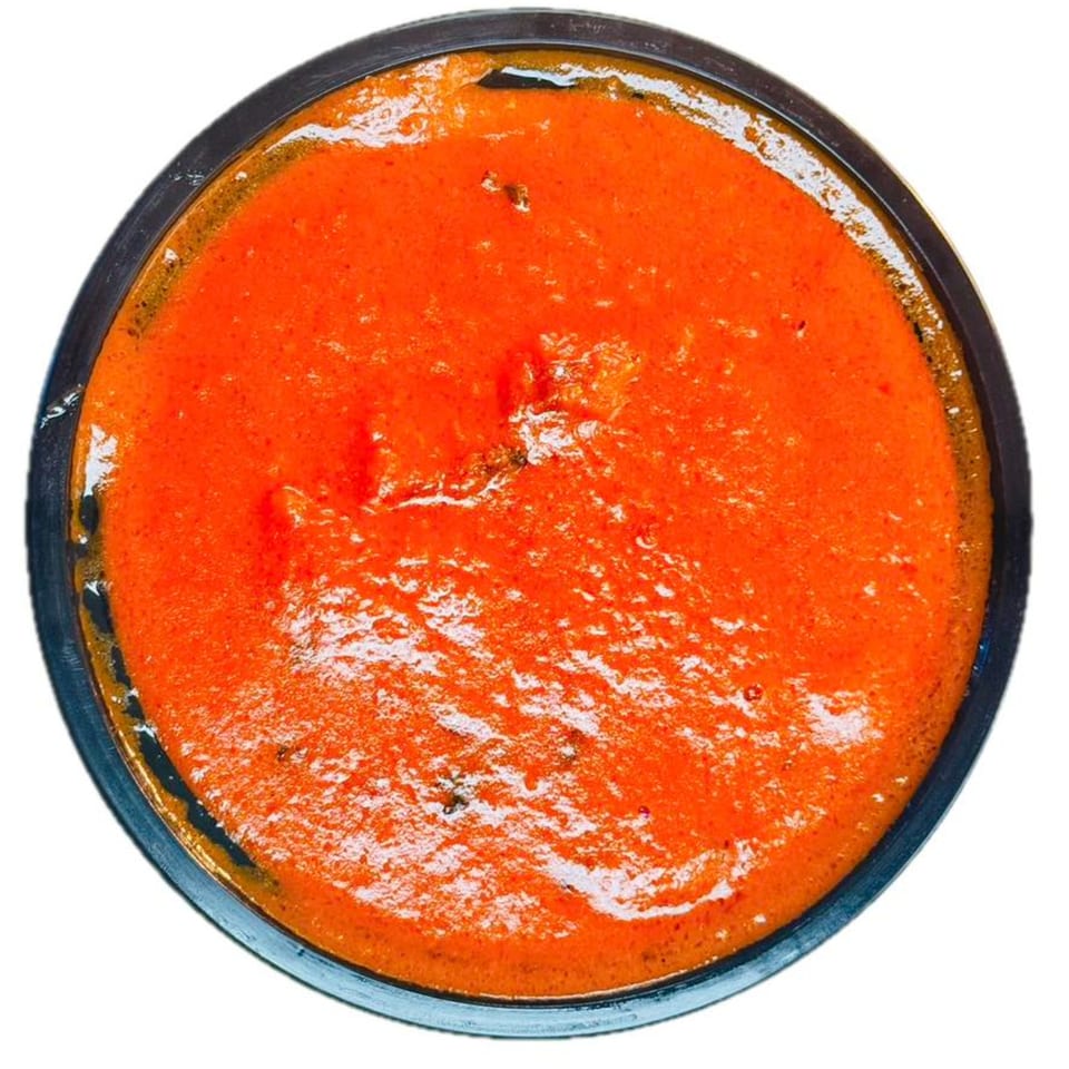 Overhead view of a bowl filled with vibrant orange-red sauce, possibly a spicy dip or soup.