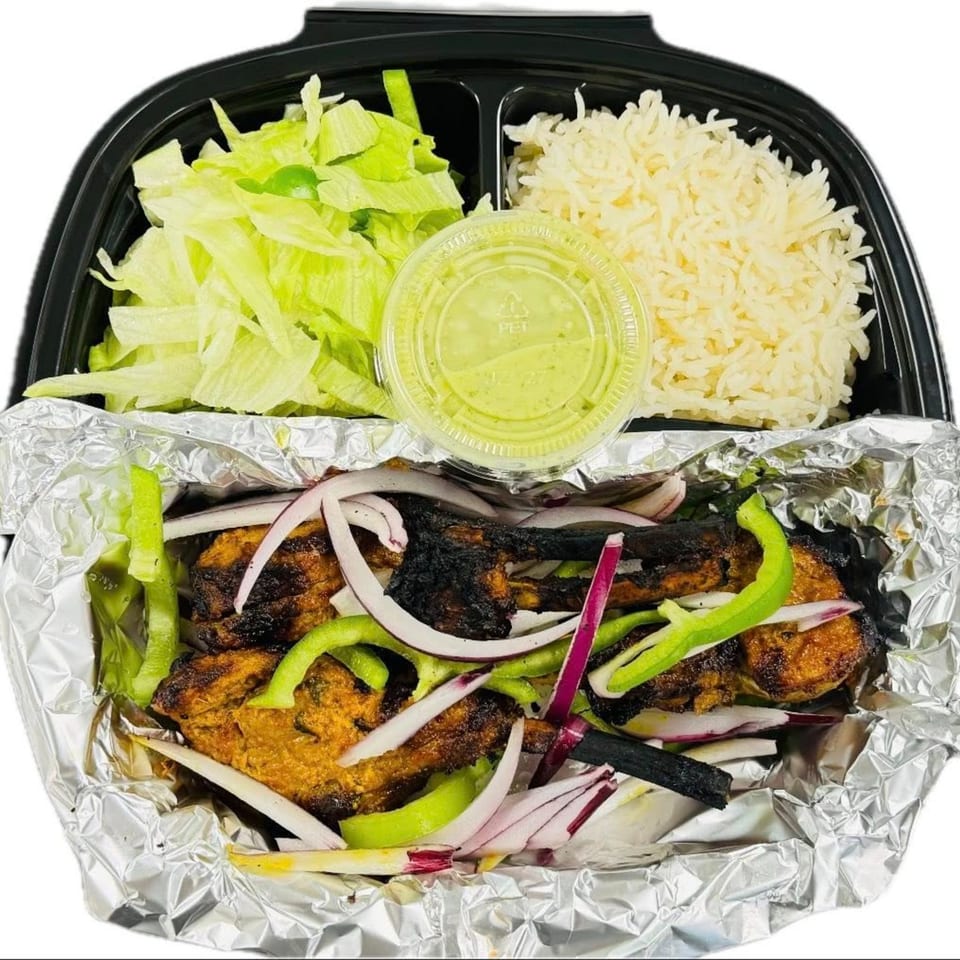 Grilled chicken with onions and peppers, rice, lettuce, and green sauce in a takeout container.
