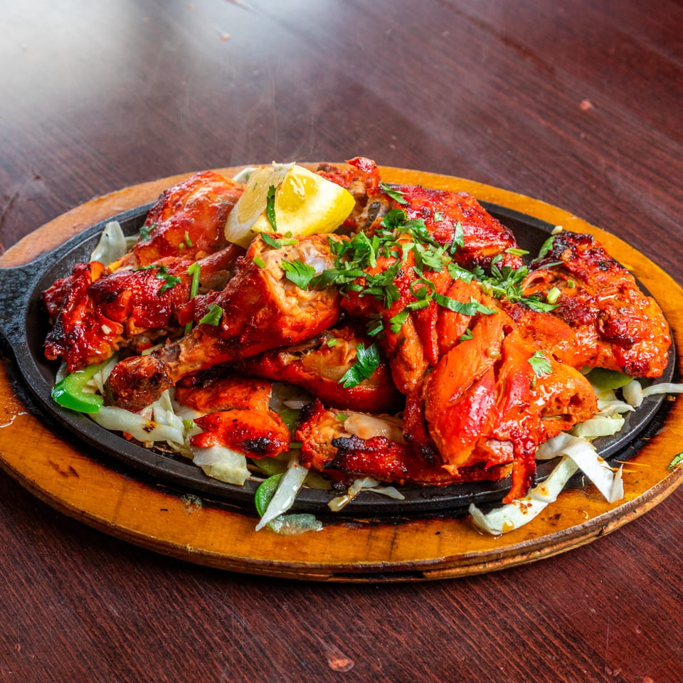 Sizzling tandoori chicken with lemon and cilantro on a hot plate.