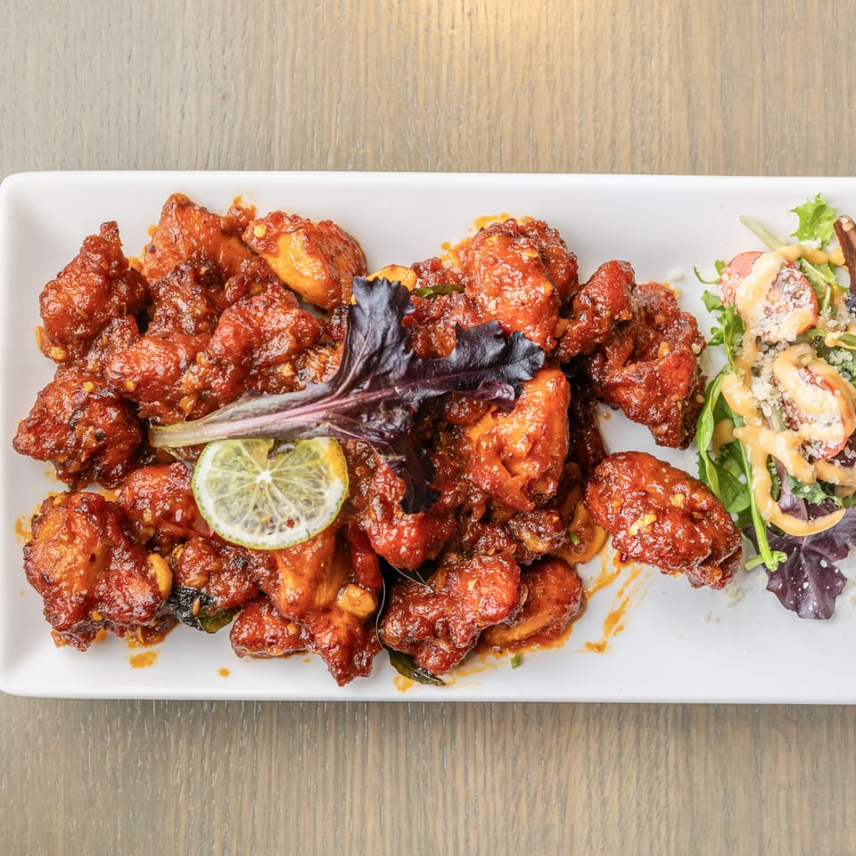 Spicy red chicken bites with a lime slice and a side salad on a white rectangular plate.