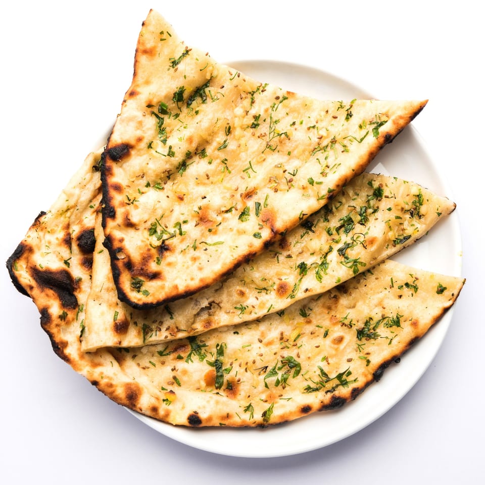 Four pieces of garlic naan bread, garnished with herbs, on a white plate.