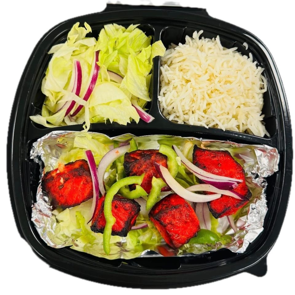 A takeout container with red chicken tikka, rice, and a side salad with lettuce and red onions.
